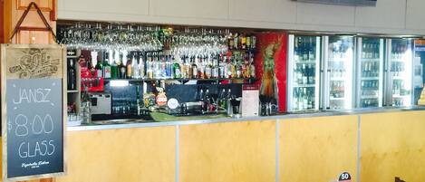 A bar area with a chalkboard sign, shelves of bottles, a cash register, and a digital screen displaying numbers.