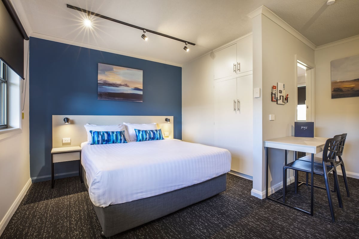 A modern hotel room with a large bed, a desk, and a chair.