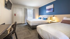 A hotel room with two beds, a desk, a TV, and a window with curtains.
