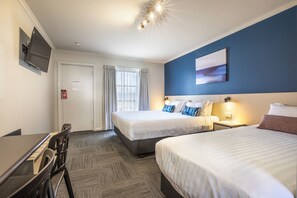 A hotel room with two beds, a desk, a TV, and a window with curtains.