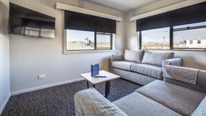 A modern living room with a grey sofa, a small table with a book and a notebook, and a flat-screen TV mounted on the wall.