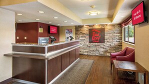 Zona de recepción de un hotel con pared de piedra, un letrero de Red Roof Inn, un letrero de RedCard y una pantalla digital para Wi-Fi gratuito.