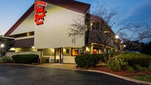 Un hotel Red Roof Inn con un diseño arquitectónico moderno, que presenta un letrero de neón llamativo, una entrada bien iluminada y un jardín delantero cuidado.