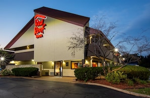 Un hotel Red Roof Inn con un diseño arquitectónico moderno, que presenta un letrero de neón llamativo, una entrada bien iluminada y un jardín delantero cuidado.