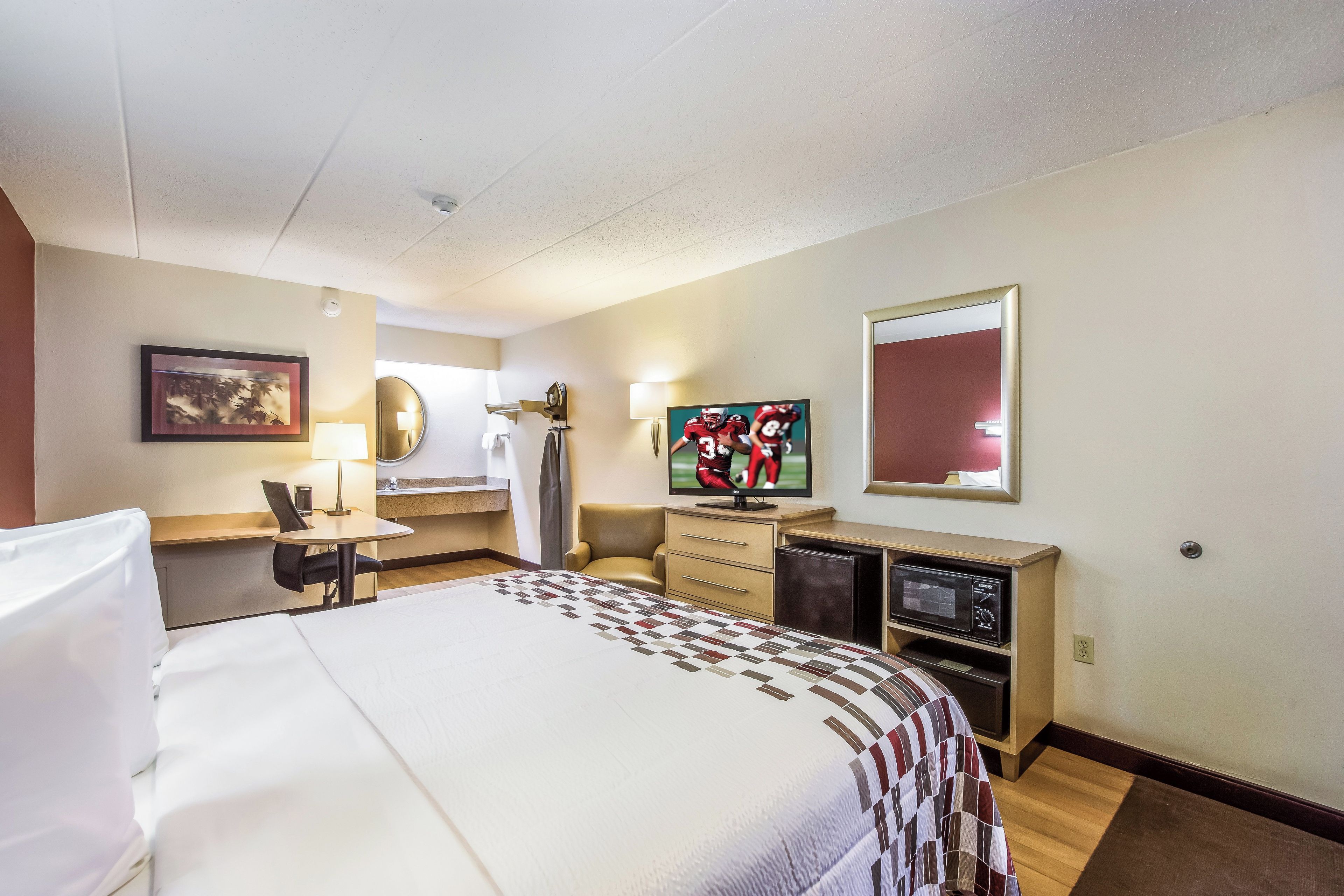 A hotel room with a bed, a desk, a television, a mirror, and a window.
