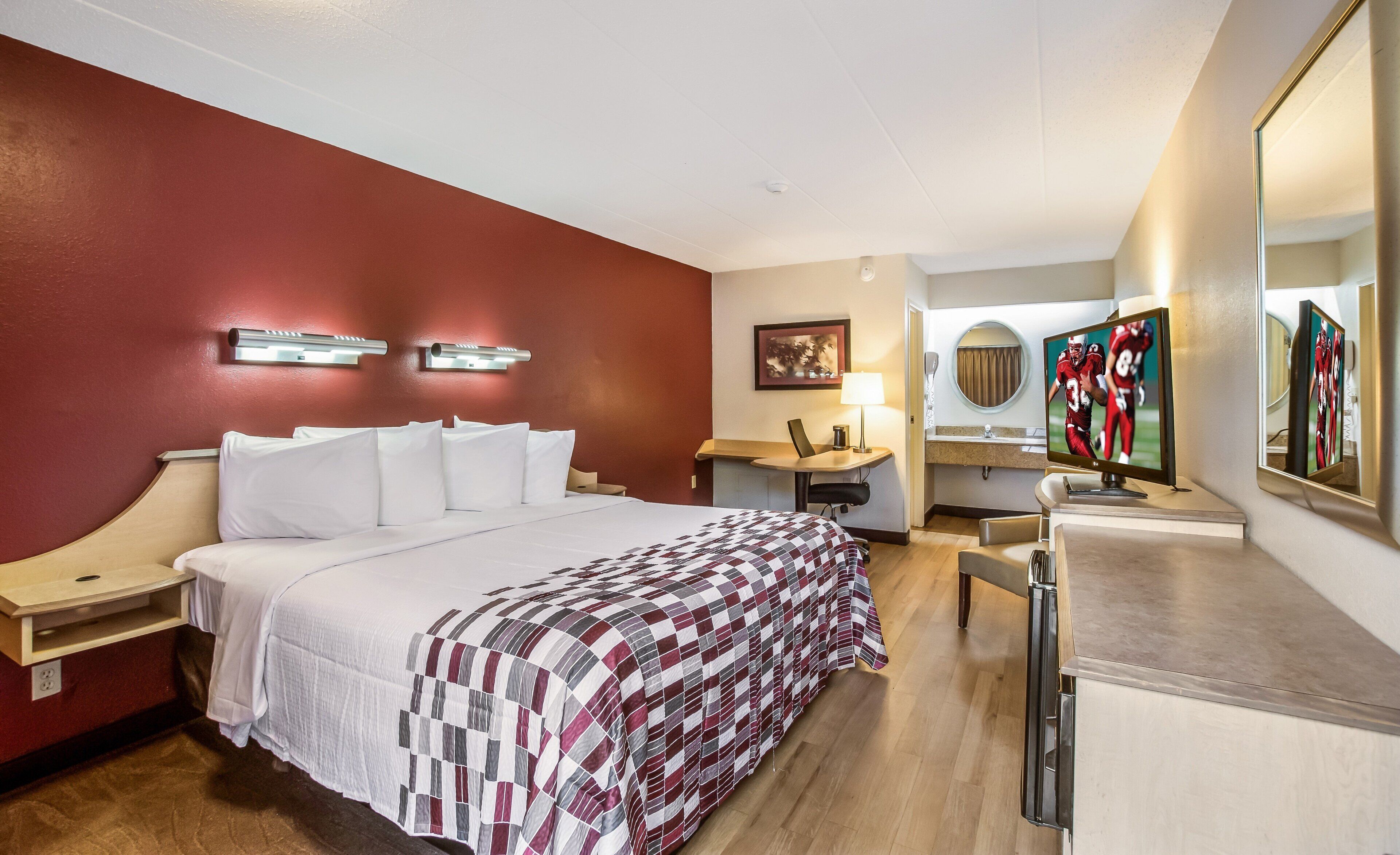 Een hotelkamer met een bed, bureau, stoel, televisie en spiegel.