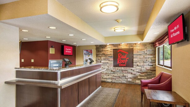 A hotel reception area with a stone wall, a Red Roof Inn sign, a Red Card sign, and a Red Chair. - Red Roof Inn Detroit - Plymouth/ Canton (Plymouth)