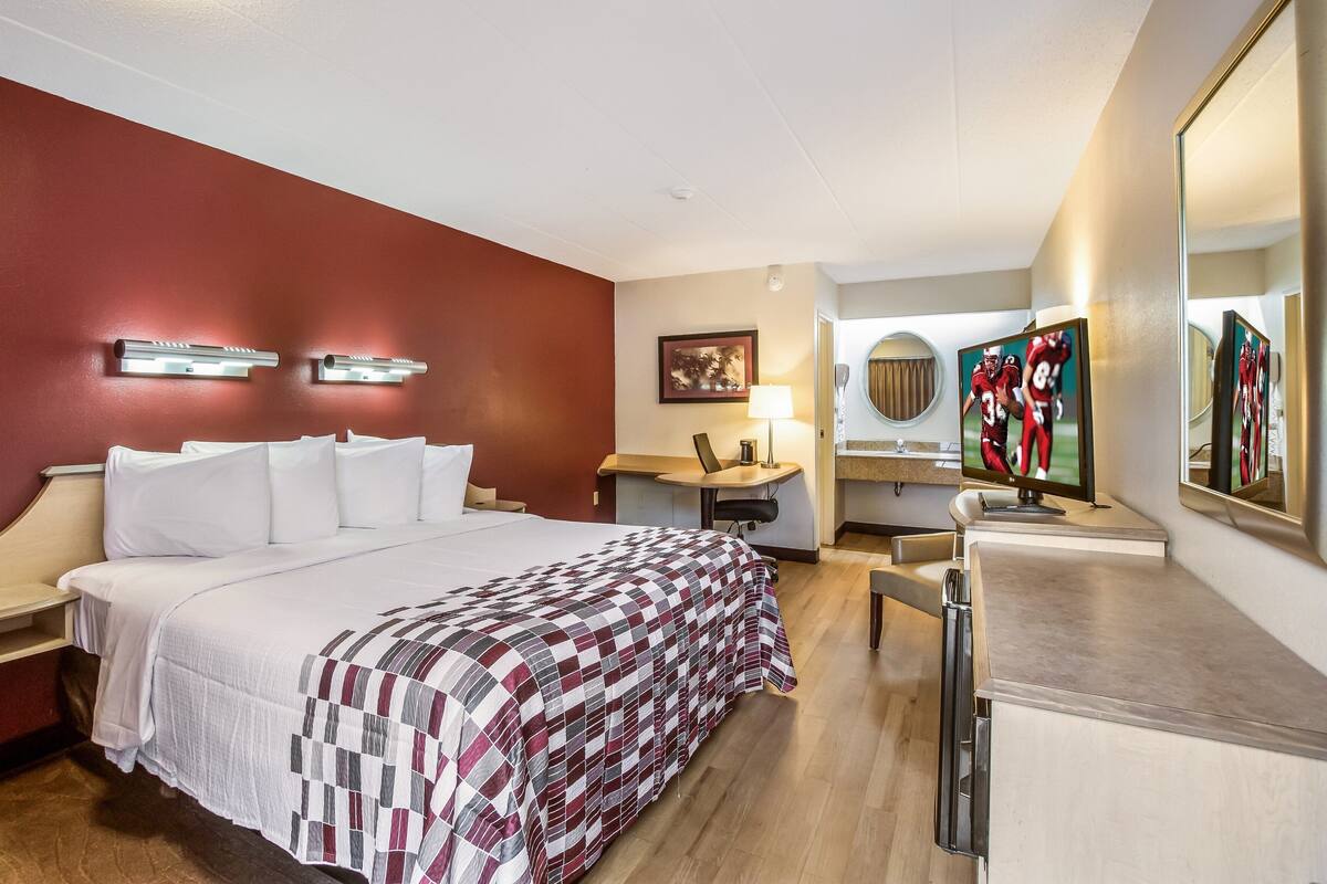 A hotel room with a bed, desk, chair, TV, and a mirror.