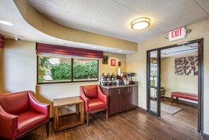 A hotel lobby with a seating area, a coffee station, and an exit sign. - Red Roof Inn Detroit - Plymouth/ Canton (Plymouth)