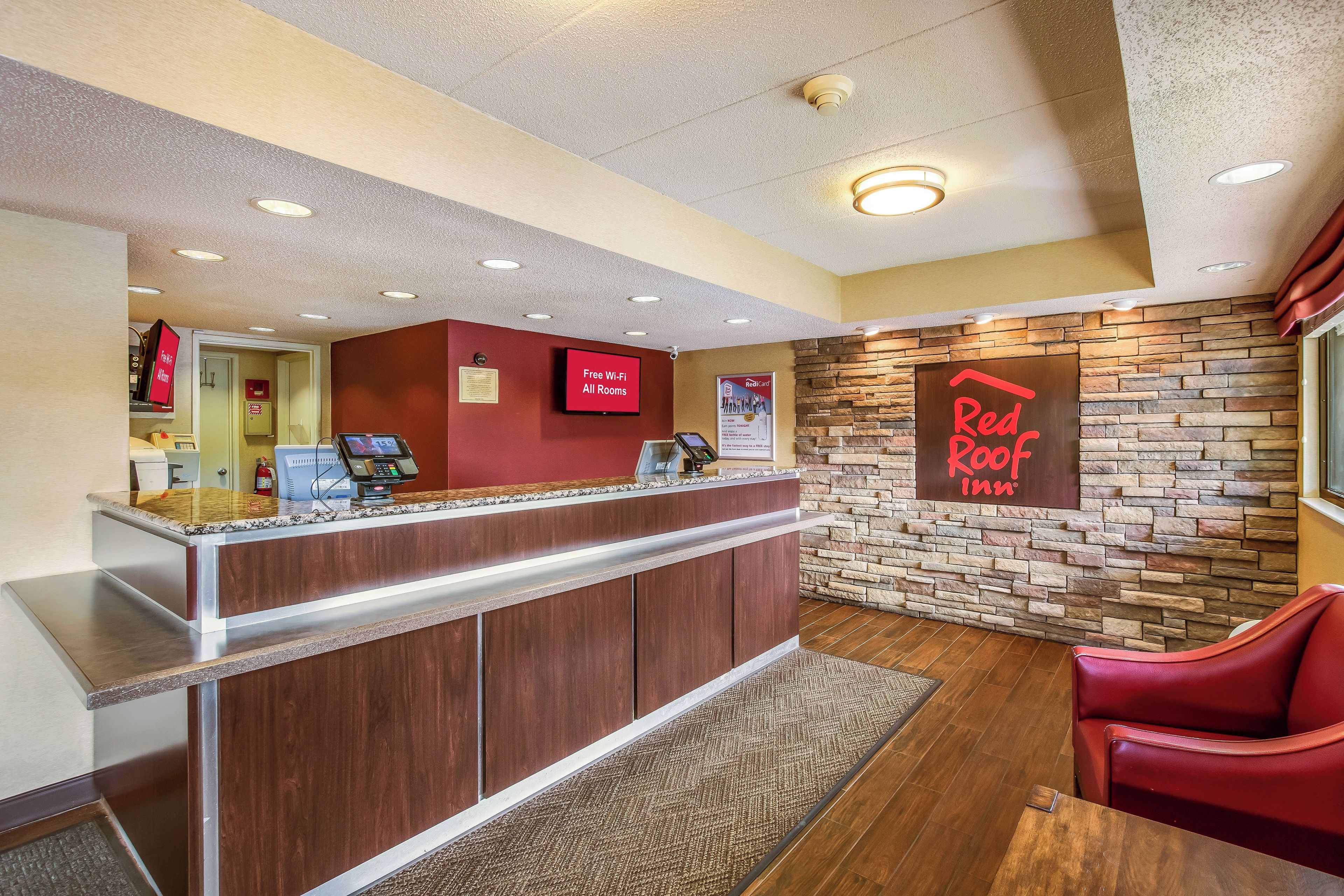 A reception area with a wooden reception desk, a Red Roof Inn sign, and a Red Roof logo on the wall.