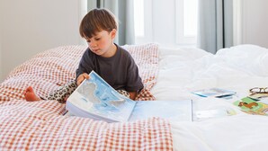 A child reading a book on a bed with checkered bedding and a window with curtains. - Alfred Hotels Paris Lecourbe - Hôtel Rénové (Paris)