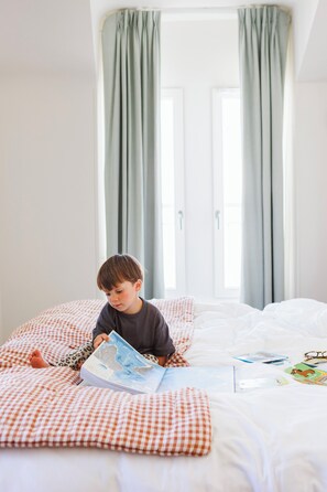 A child reading a book on a bed with checkered bedding and a window with curtains. - Alfred Hotels Paris Lecourbe - Hôtel Rénové (Paris)