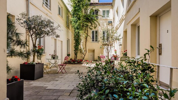 A narrow courtyard with tiled flooring, potted plants, and outdoor seating. - Alfred Hotels Paris Lecourbe - Hôtel Rénové (Paris)