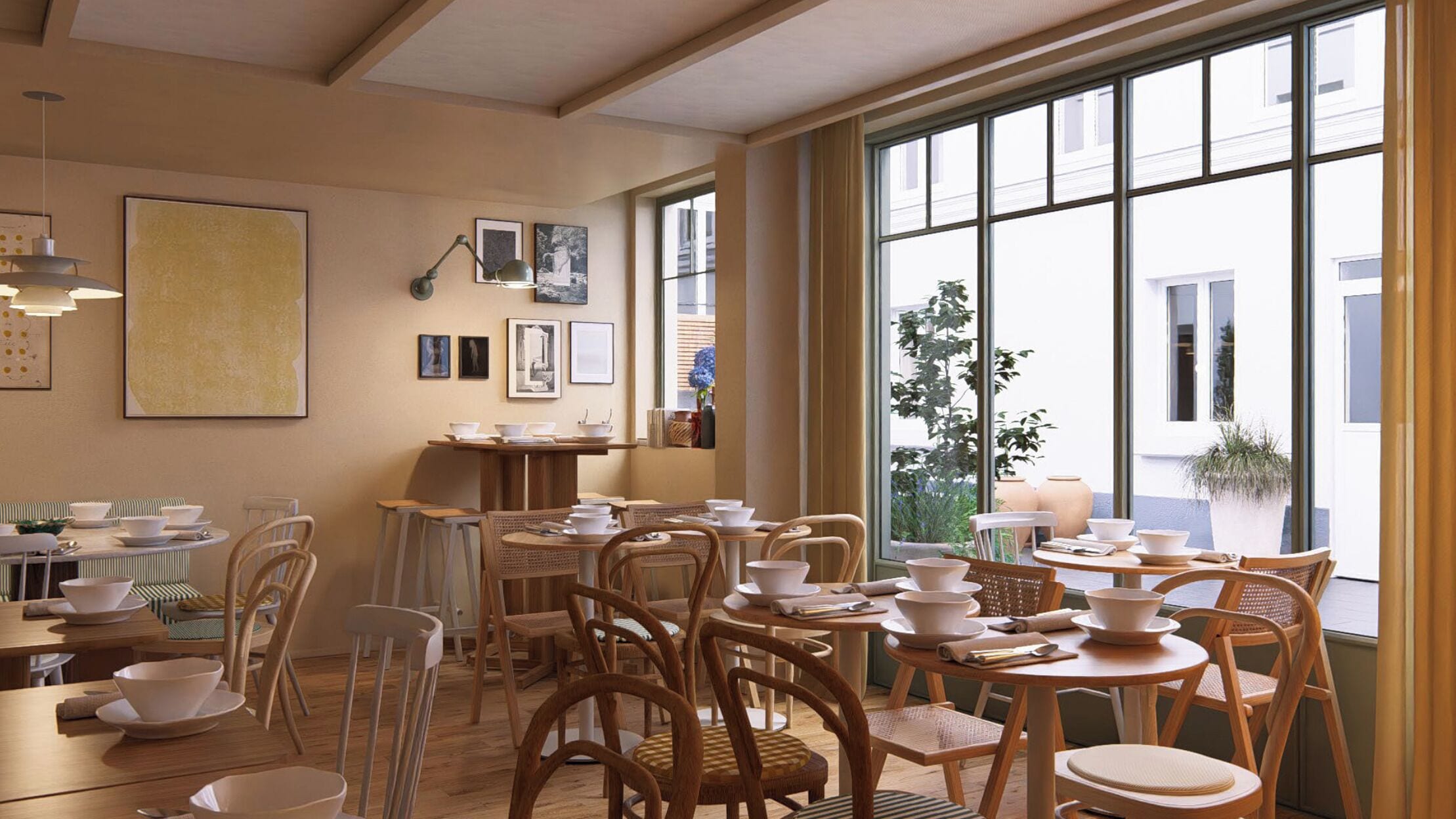 A dining area with multiple tables and chairs, framed artwork on the walls, and large windows offering a view of the outside.