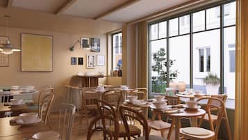 A dining area with multiple tables and chairs, framed artwork on the walls, and large windows offering a view of the outside.