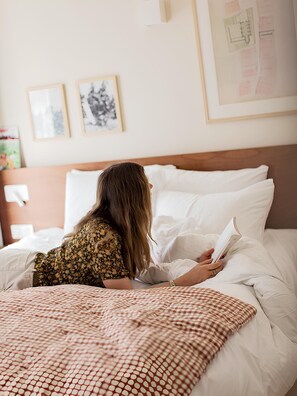 A person lying on a bed with a checkered blanket, reading a book. The room has a wooden headboard, white bedding, and two framed pictures on the wall. - Alfred Hotels Paris Lecourbe - Hôtel Rénové (Paris)