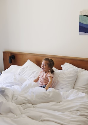 A child sitting on a bed with white bedding and a wooden headboard. - Alfred Hotels Paris Lecourbe - Hôtel Rénové (Paris)