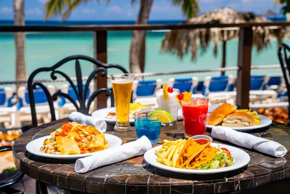 A dining table with plates of food, drinks, and a view of the ocean.