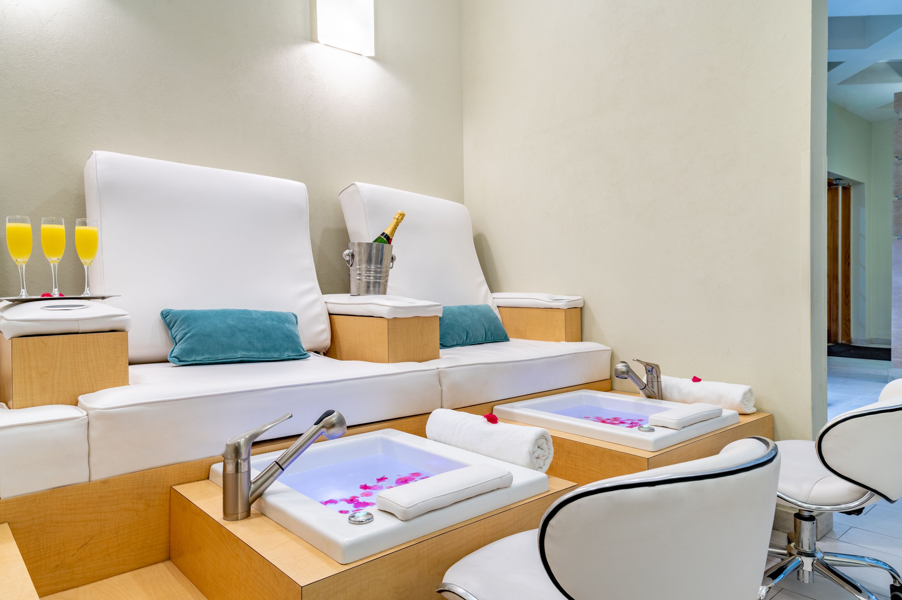 A spa area with two large white sofas, a small sink with a mirror, and three glasses of orange juice.