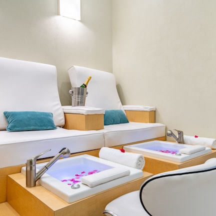 A spa area with two large white sofas, a small sink with a mirror, and three glasses of orange juice.
