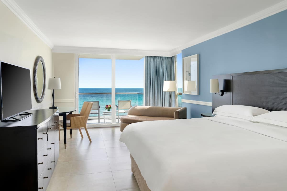 Una camera d'albergo con un letto grande, una scrivania con una sedia, una televisione e vista sull'oceano.