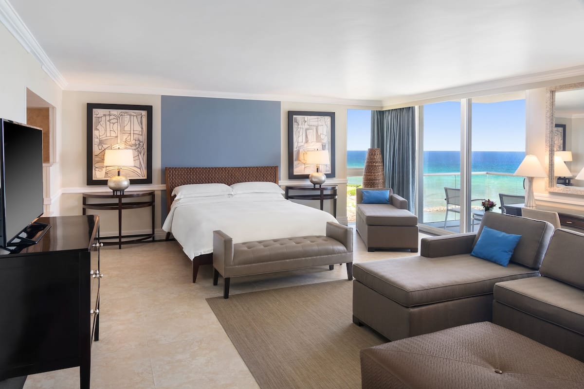 Una camera d'albergo con un letto, un divano, una televisione e vista sull'oceano.