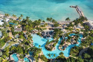An aerial view of a resort with multiple swimming pools, palm trees, and a beach area.