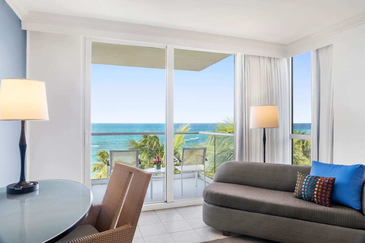 Un balcone con vista sull'oceano, un divano con un cuscino decorato e un tavolo con una lampada.