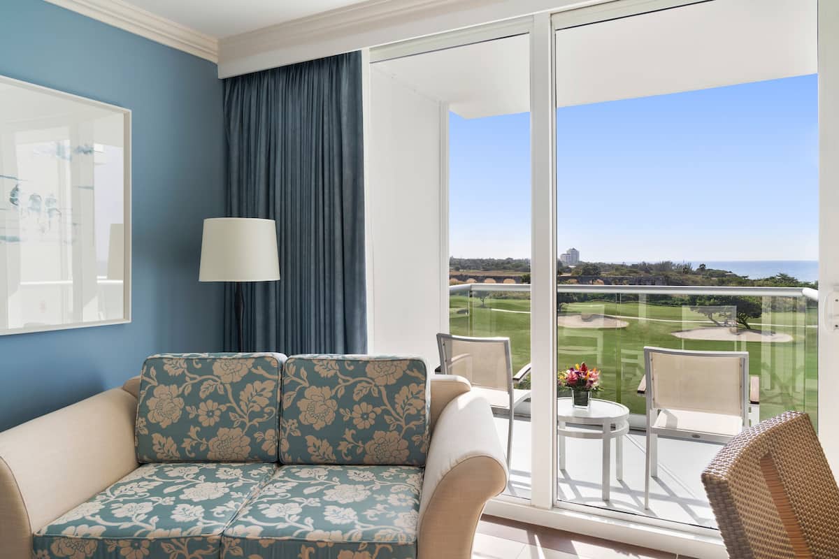 Un balcone con vista su un campo da golf, un divano, un tavolo con un vaso e una sedia.