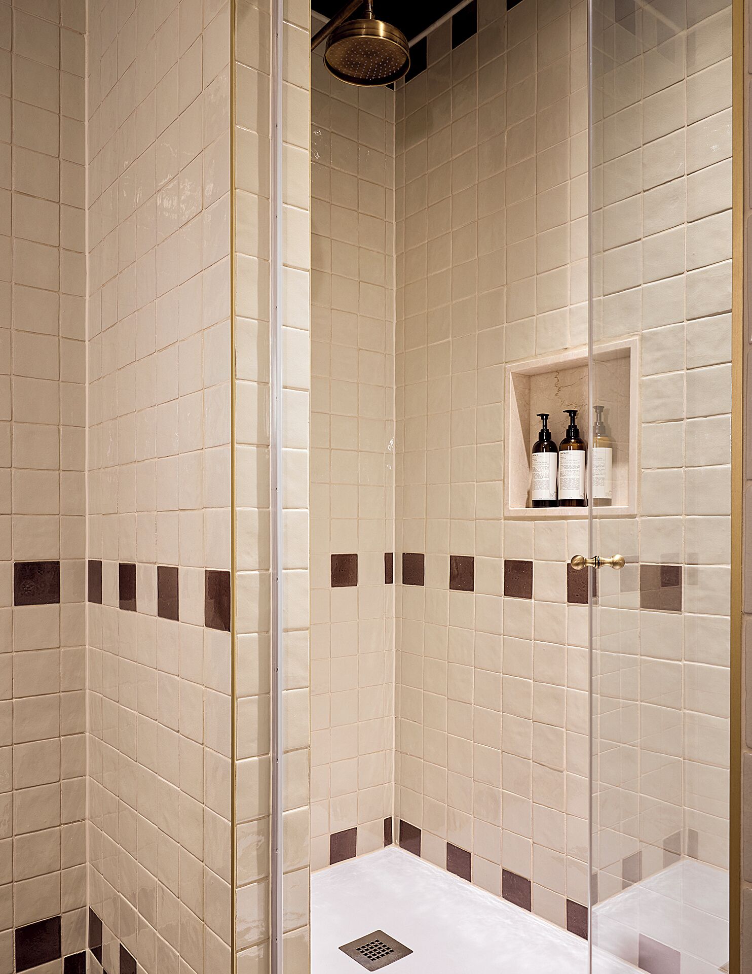 Una ducha con azulejos, una puerta de cristal, un cabezal de ducha y un estante con artículos de aseo.