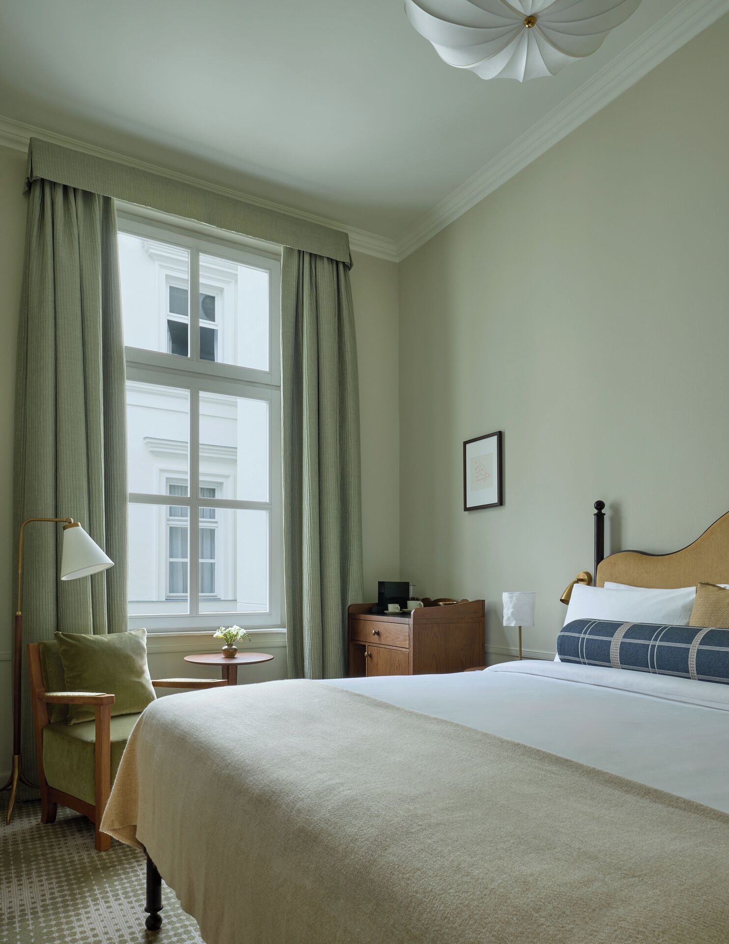 Habitación de hotel con una cama grande, un escritorio, una silla, una lámpara y una ventana con cortinas.