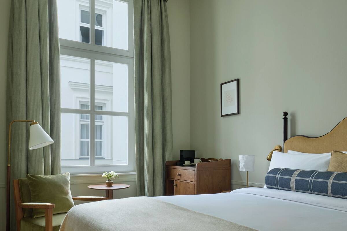 A hotel room with a large bed, a desk, a chair, a lamp, and a window with curtains.