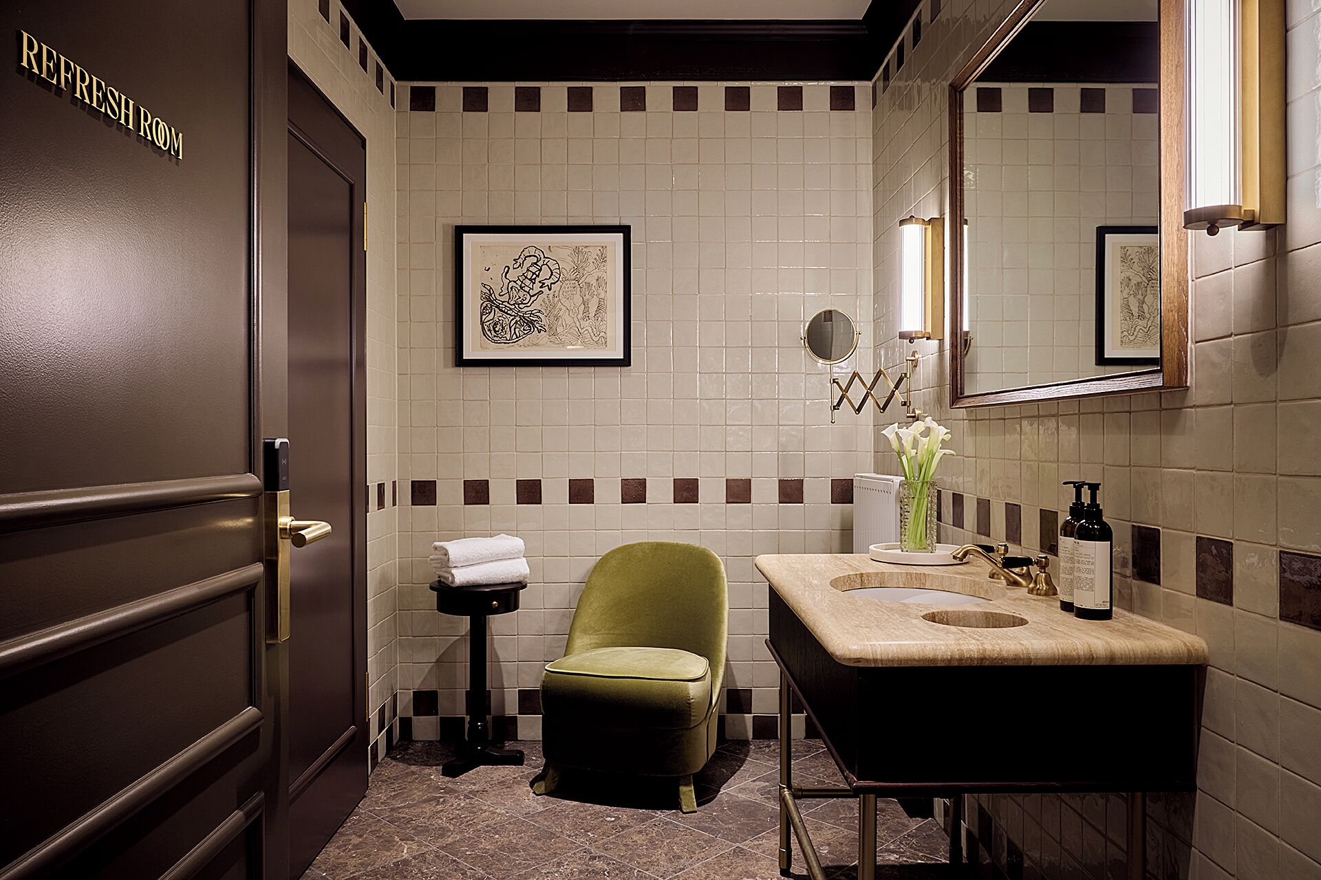 Un bagno con un lavabo, una sedia, un piccolo tavolo con asciugamani e opere d'arte incorniciate appese al muro.