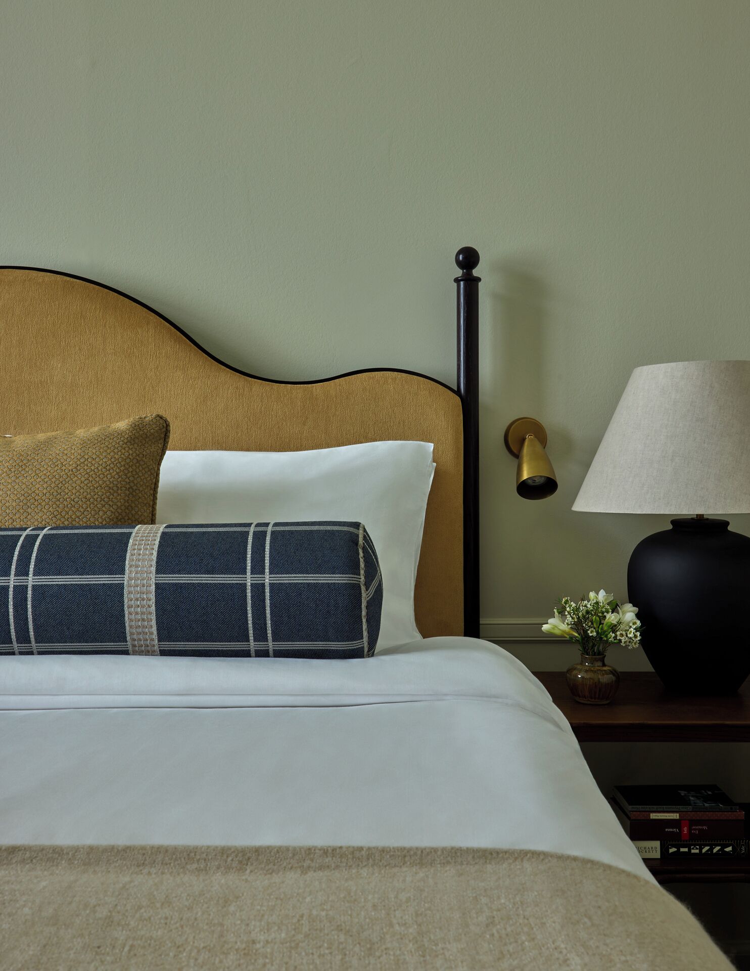 A neatly made bed with a headboard, a bedside lamp, and a small vase with flowers.