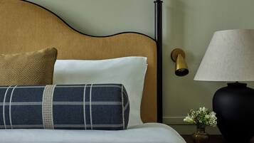 A neatly made bed with a headboard, a bedside lamp, and a small vase with flowers.