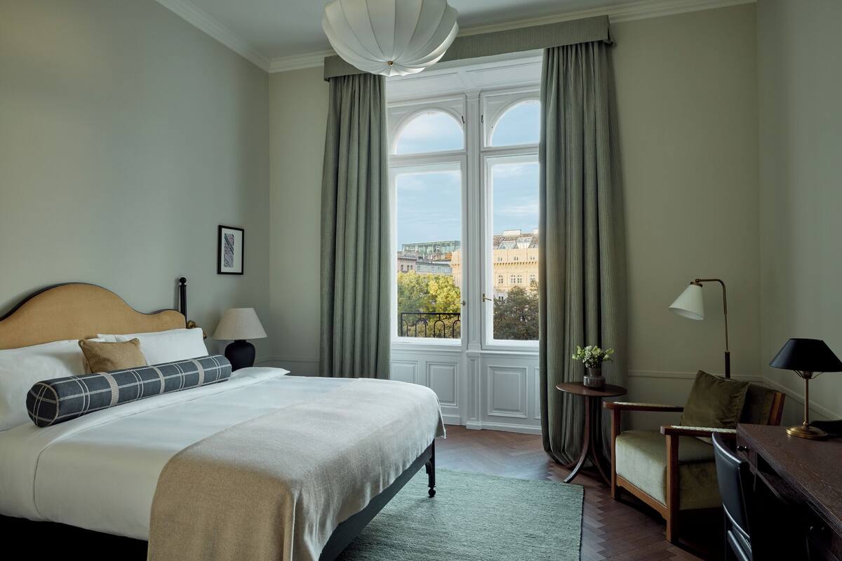 Habitación de hotel con una cama grande, una silla, un escritorio y vista a la ciudad a través de una ventana.