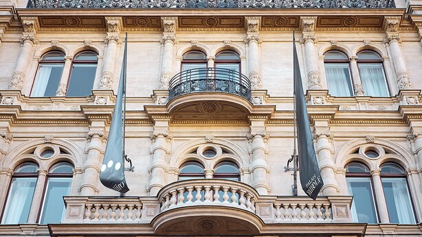 Ein Gebäude mit aufwendigen architektonischen Details, darunter Säulen, Bögen und ein Balkon mit einem Balustraden.