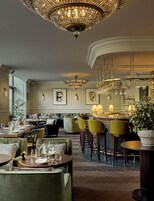 Uma sala de jantar ampla, com várias mesas e cadeiras, lustres elegantes e ambiente bem iluminado.