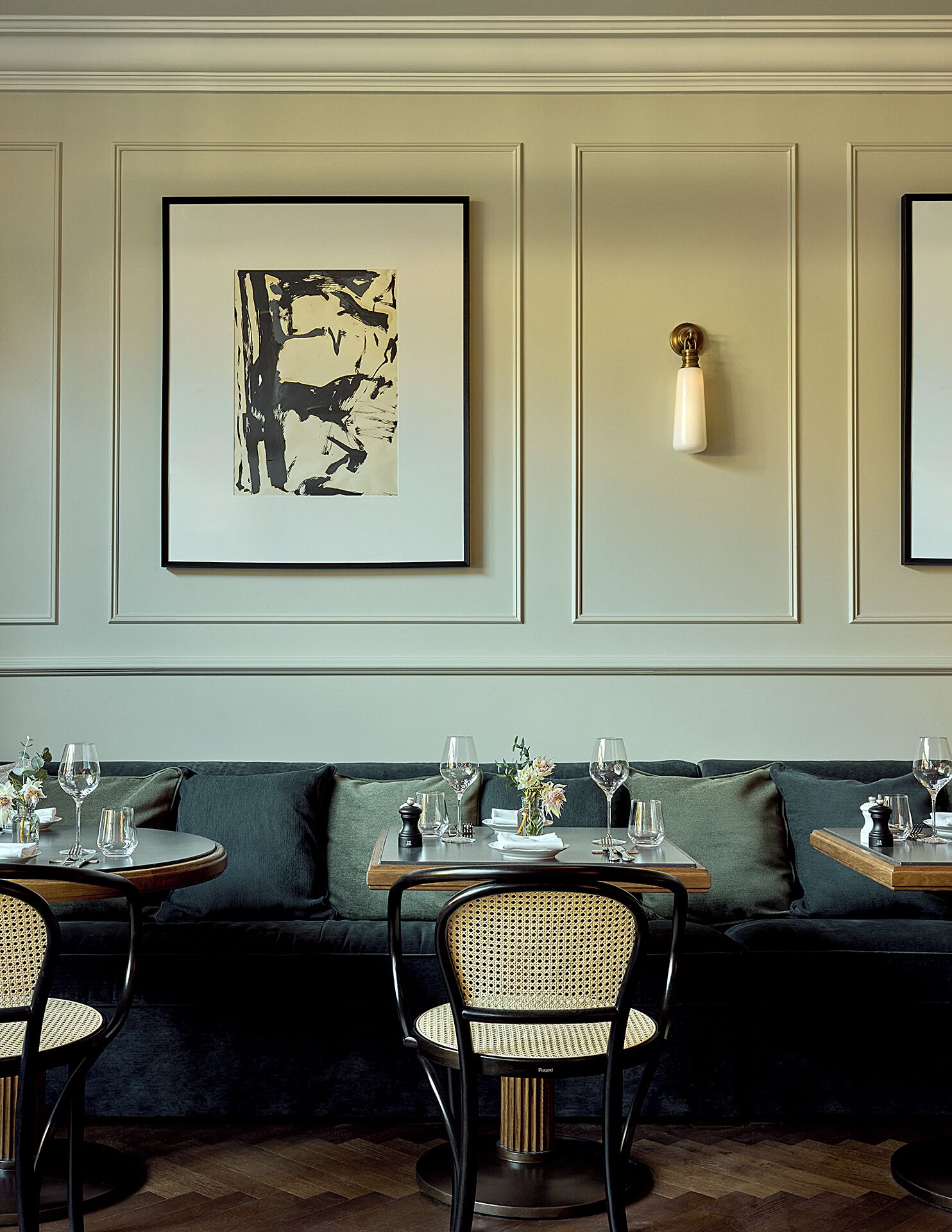Una sala da pranzo con un divano verde, due tavoli tondi, sedie in vimini e opere d'arte incorniciate al muro.