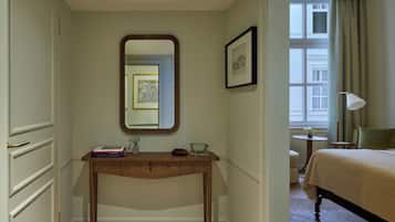 Una camera d'albergo con una scrivania in legno, uno specchio, un quadro incorniciato, un letto, una lampada e una finestra con tende.