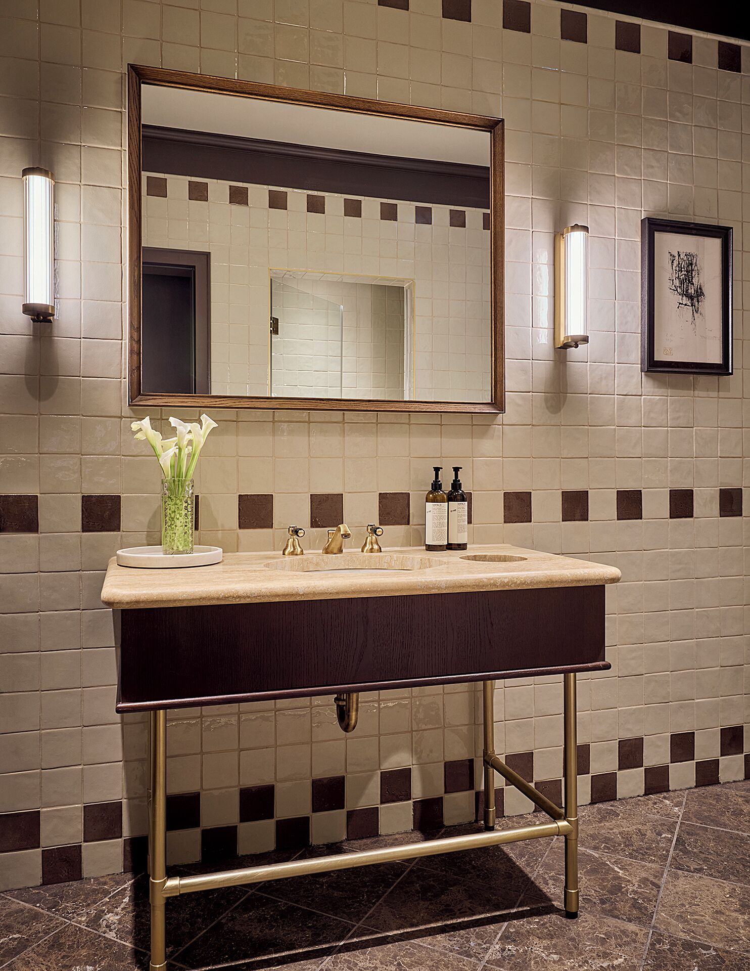 Un baño con un espejo grande, un lavabo con dos grifos y un jarrón con flores.