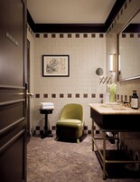 Een badkamer met een groene stoel, een wastafel met spiegel en een kunstwerk in een lijst aan de muur.