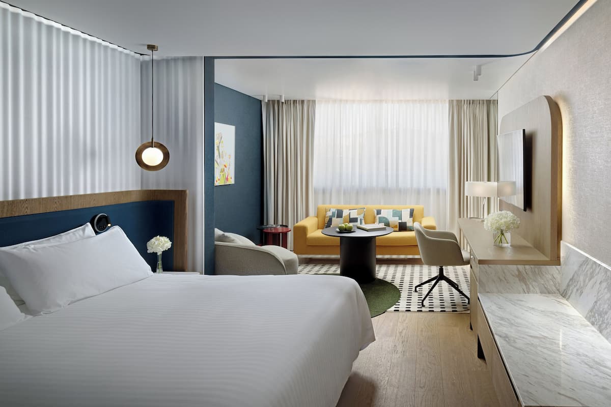 A hotel room with a large bed, a sofa, a small round table, and a desk with a lamp.