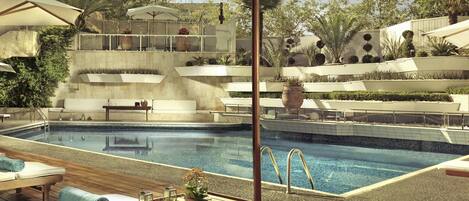 A poolside area with lounge chairs, a wooden table, and umbrellas.