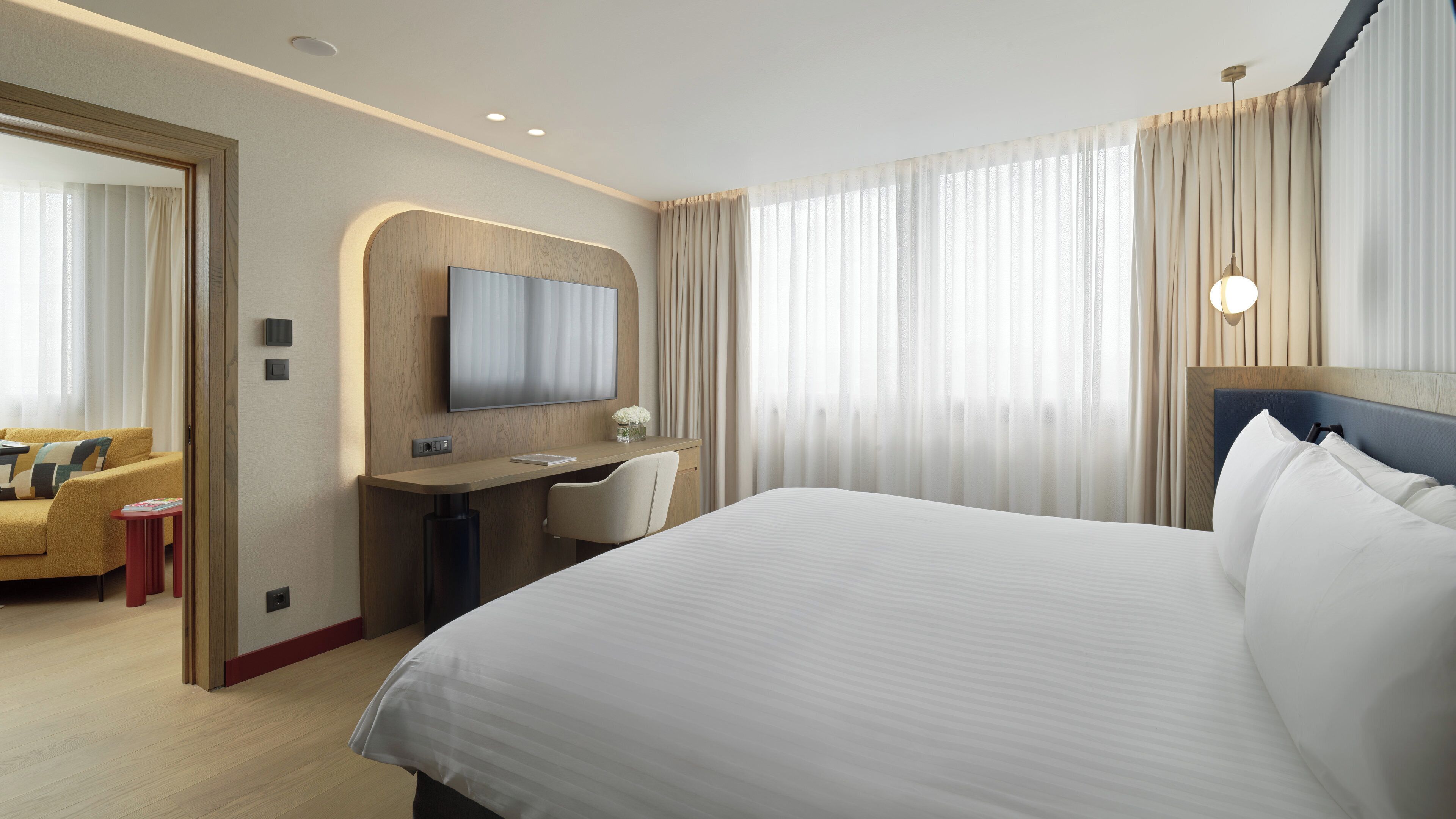 Une chambre d’hôtel avec un grand lit, un bureau avec une chaise, une télévision et un miroir.