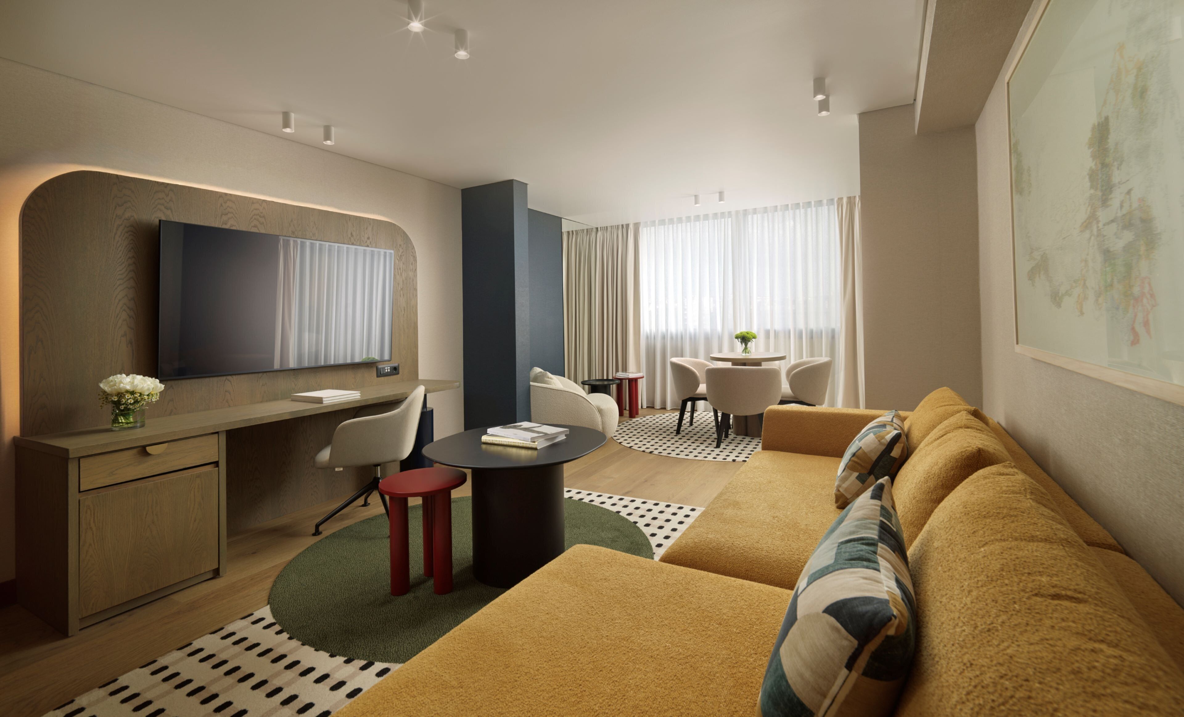 A modern hotel room with a sofa, a TV, a desk, and a dining area.