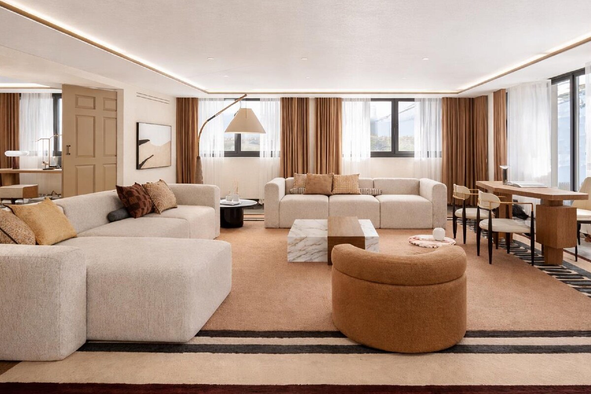 A modern living room with a sectional sofa, ottoman, and a dining area with chairs and a table.