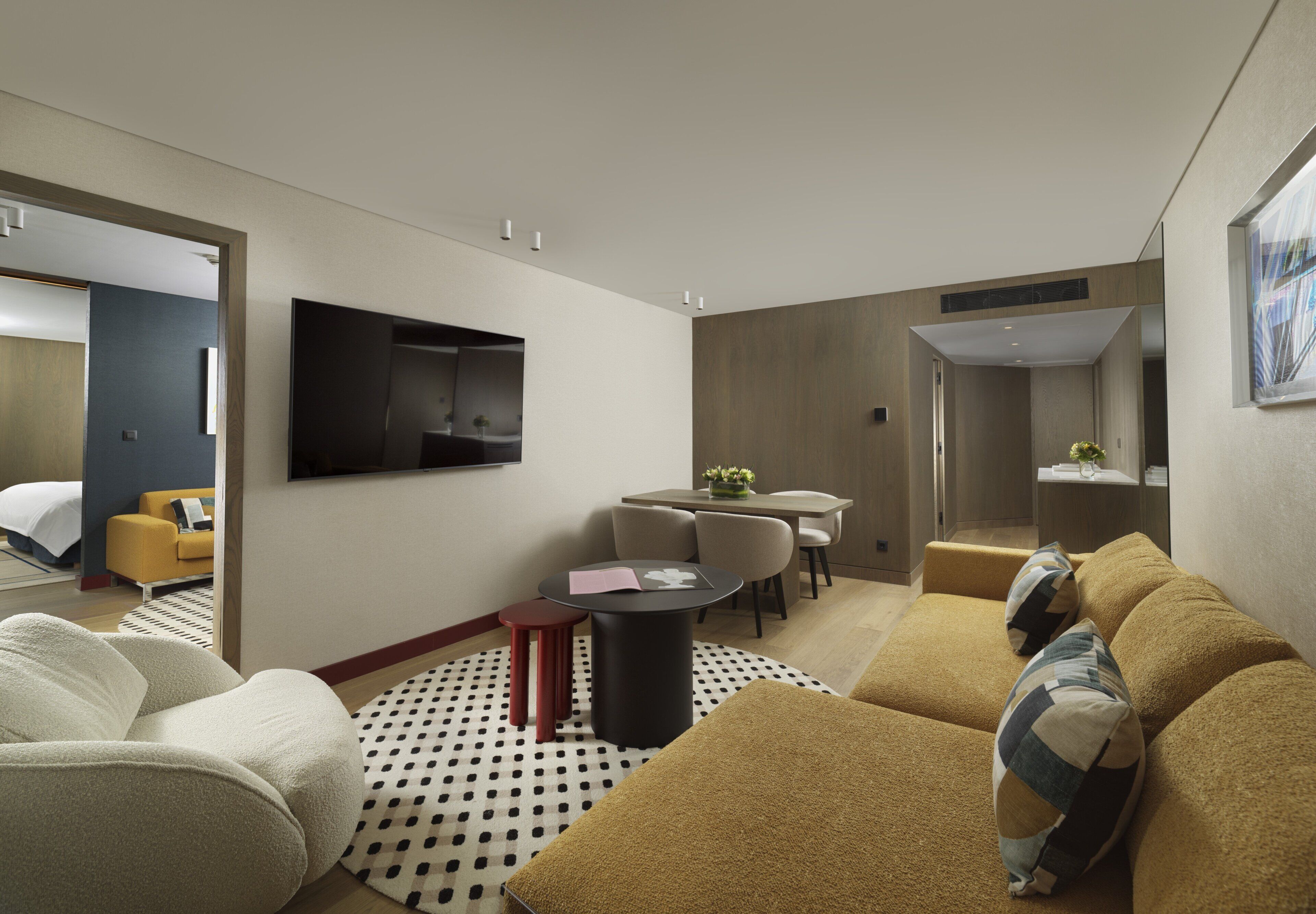 Quarto de hotel moderno com sofá, área de refeições e televisão na parede.