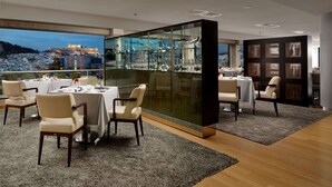 A modern dining area with tables set for two, a glass partition with decorative items, and a view of a historic cityscape.