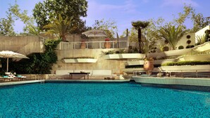 A swimming pool with lounge chairs and umbrellas, surrounded by greenery and a tiered garden.